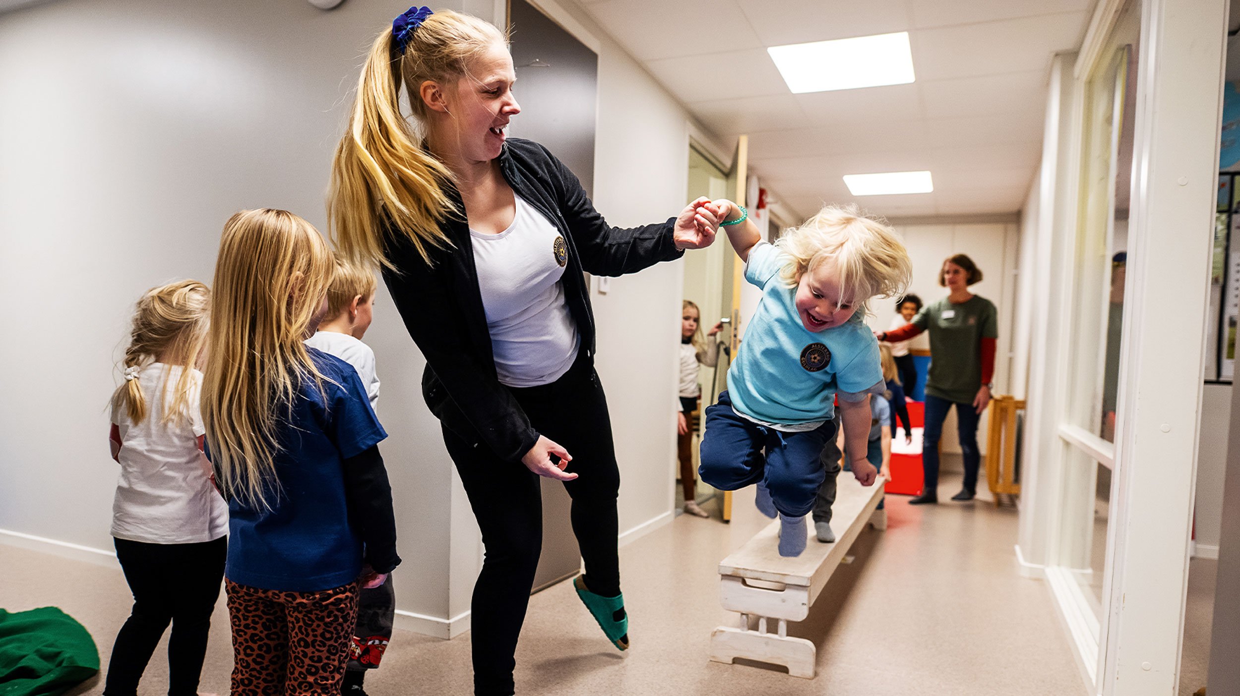 Läraren i förskolan Sanna Petersson ger stöd när Elvira hoppar från en bänk i förskolans egna hinderbana.