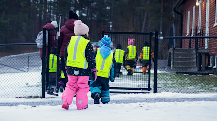 Förskolebarn med reflexvästar går in på en förskolegård.