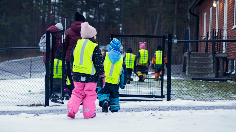 Förskolebarn med reflexvästar går in på en förskolegård.