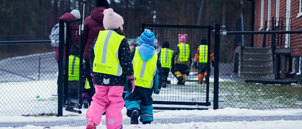 Förskolebarn med reflexvästar går in på en förskolegård.