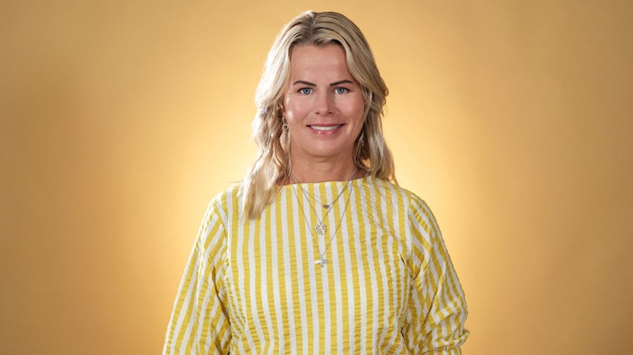 Ett porträtt av Anna Olskog, som ser glad ut, mot gul bakgrund, i en gulrandig klänning