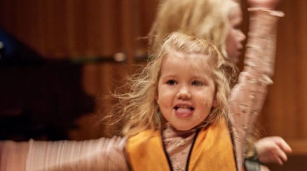 Ett litet barn dansar koncentrerat och ett annat barn skymtar i bakgrunden.