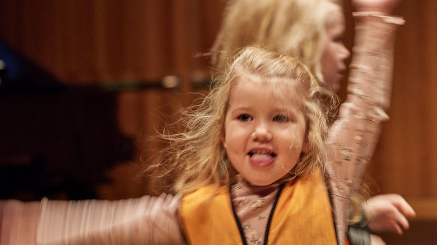 Ett litet barn dansar koncentrerat och ett annat barn skymtar i bakgrunden.