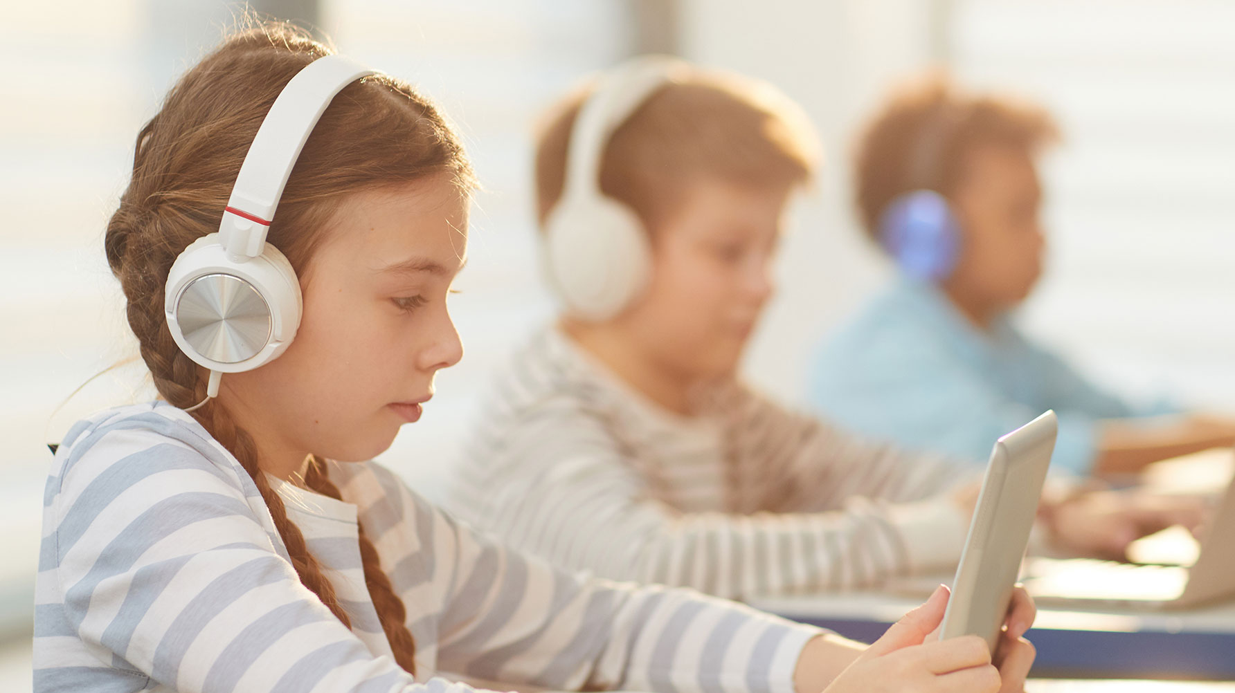 En genrebild av tre elever med skärmar framför sig, samtliga tre har hörlurar