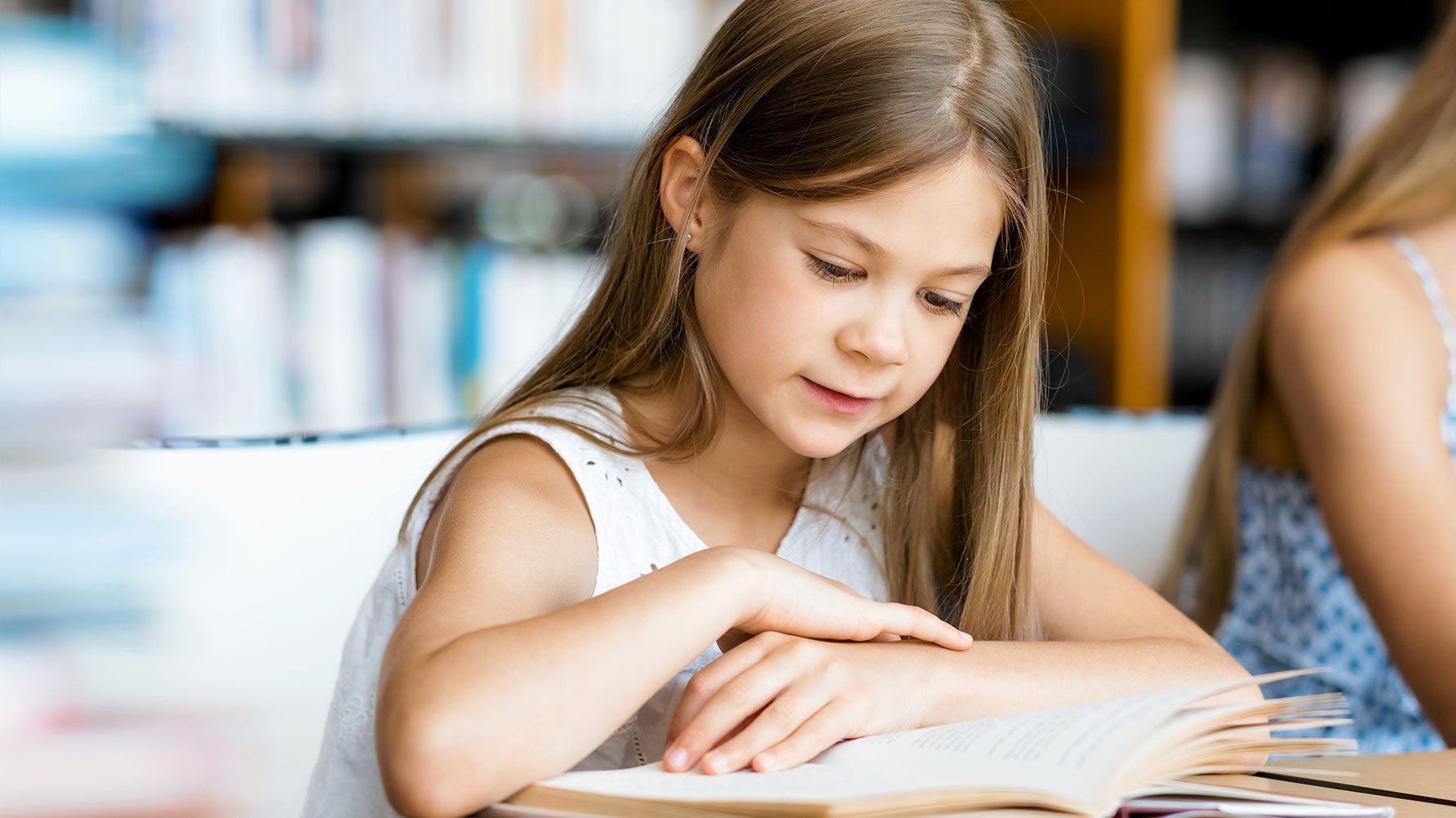 En genrebild av en flicka som läser i en bok som ligger uppslagen på bordet framför sig