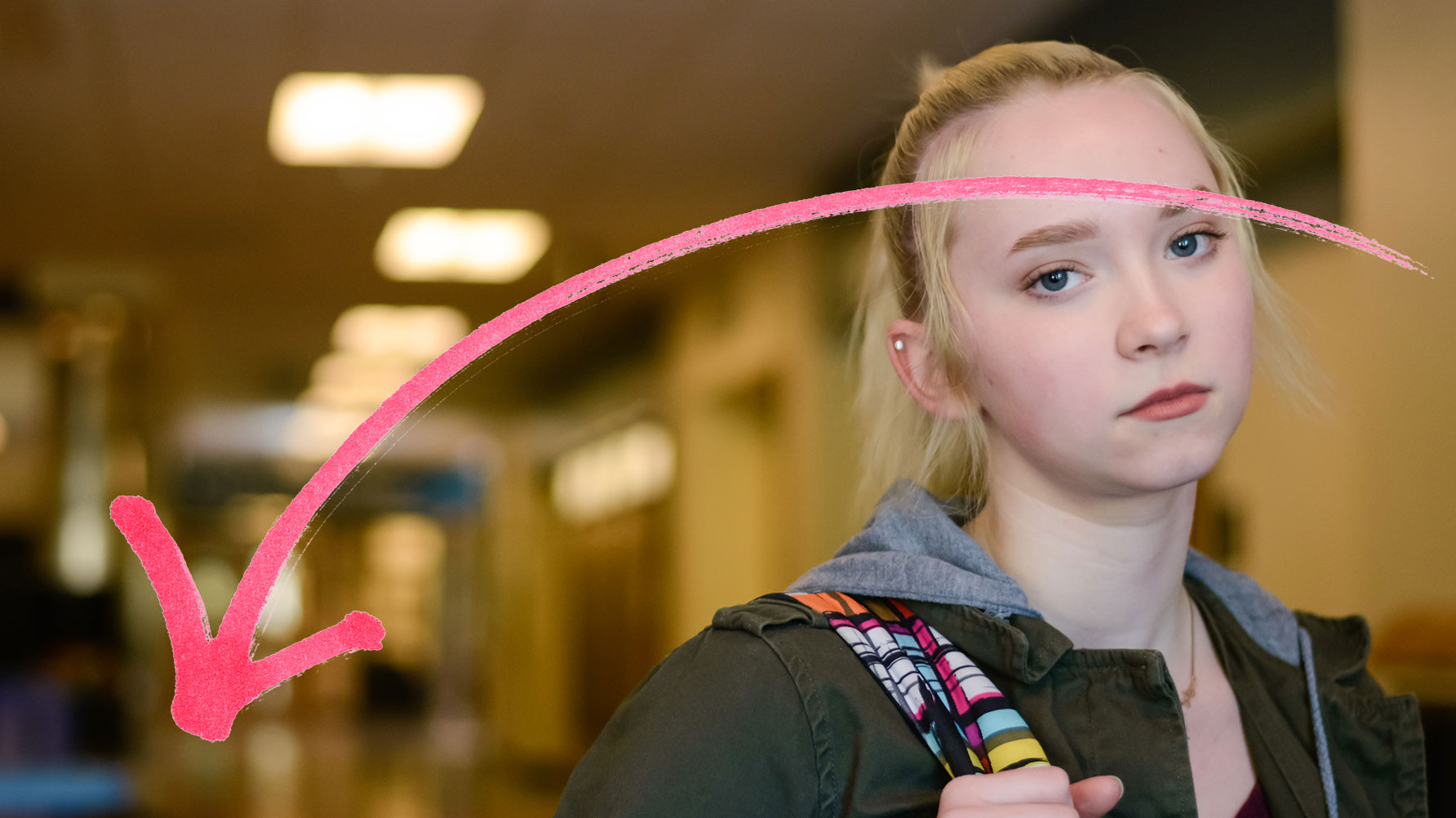 En genrebild av en allvarlig flicka i skolkorridor, en röd pil över hennes ansikte pekar nedåt