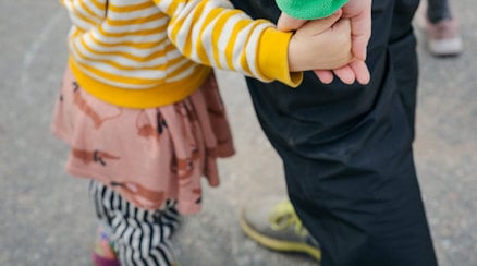 Ett litet barn håller en lärare i handen, man ser lärarens sko