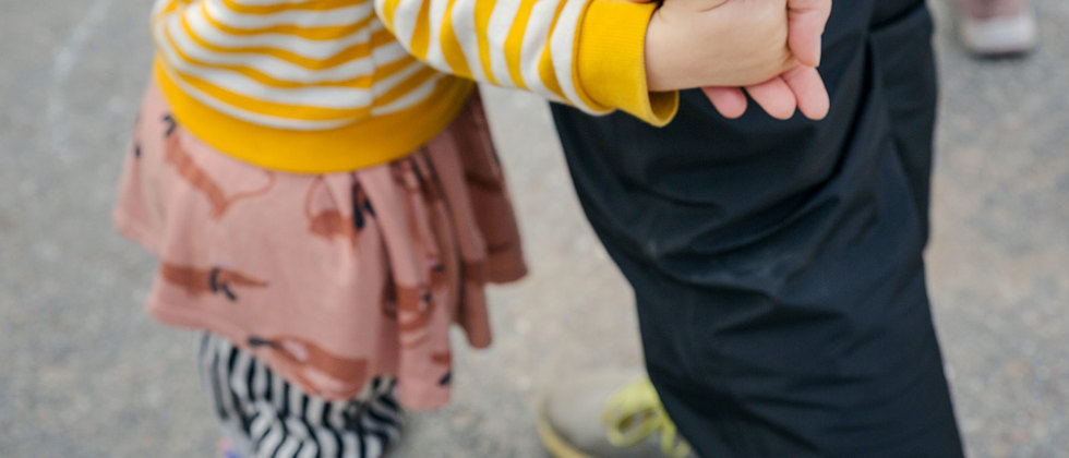 Ett litet barn håller en lärare i handen, man ser lärarens sko