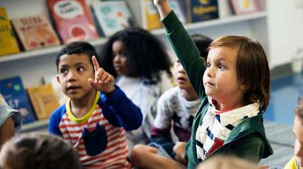 En grupp barn som lyssnar uppmärksamt, ett barn räcker upp handen