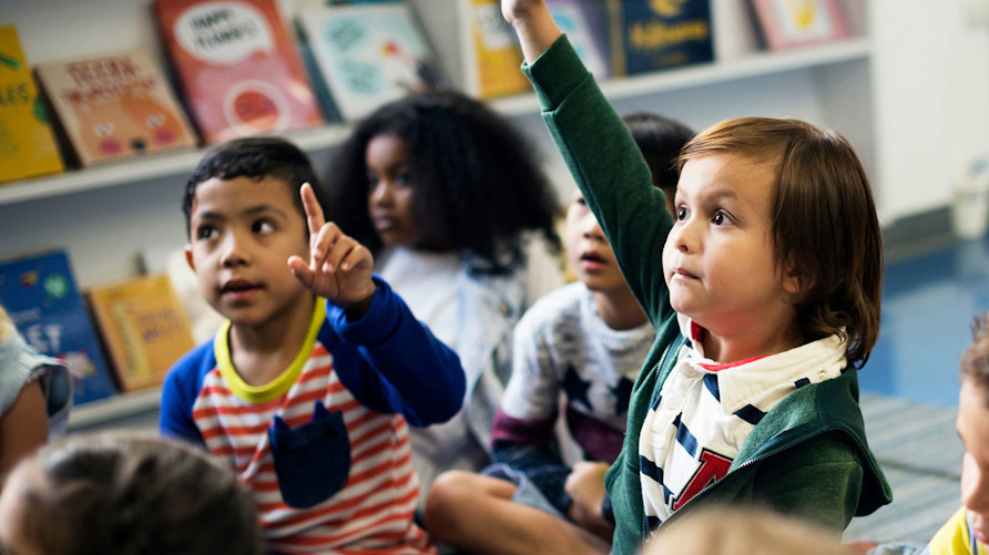 En grupp barn som lyssnar uppmärksamt, ett barn räcker upp handen
