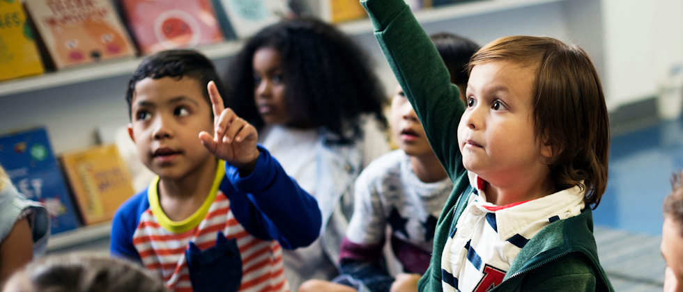 En grupp barn som lyssnar uppmärksamt, ett barn räcker upp handen