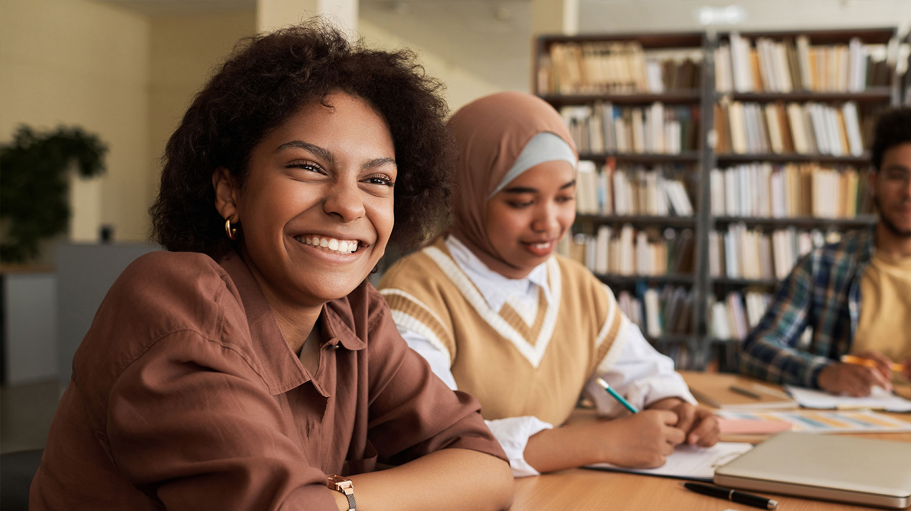 En genrebild av tre elever som sitter med papper framför sig på bordet, en bär hijab.