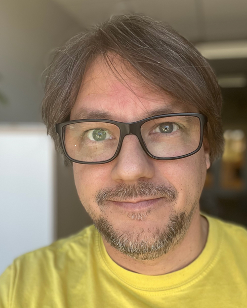 Ett porträtt av John Bang i glasögon och gul tröja