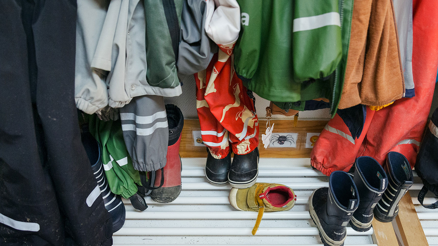 Ett fotografi fr&#xE5;n kapprummet p&#xE5; en f&#xF6;rskola, h&#xE4;ngande f&#xE4;rgglada regnkl&#xE4;der och leriga st&#xF6;vlar under dem.