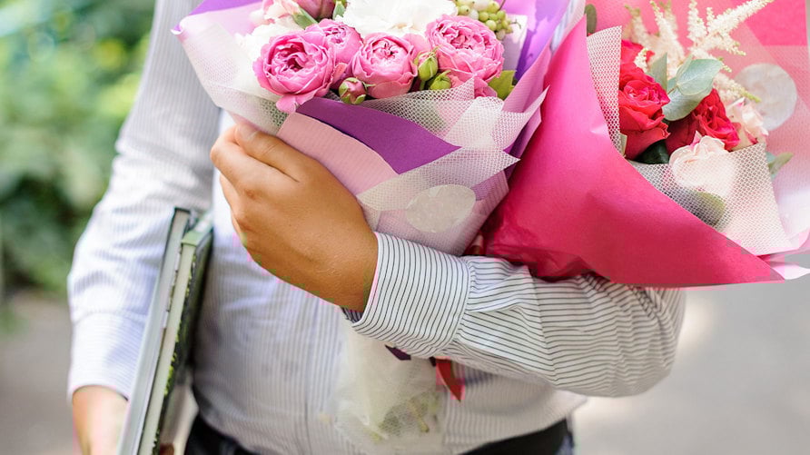 En man i skjorta med böcker under ena armen och två blombuketter