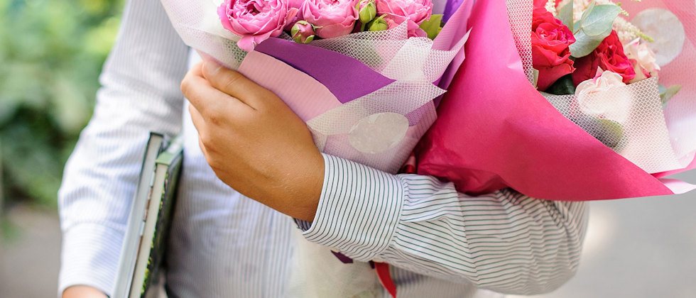 En man i skjorta med böcker under ena armen och två blombuketter