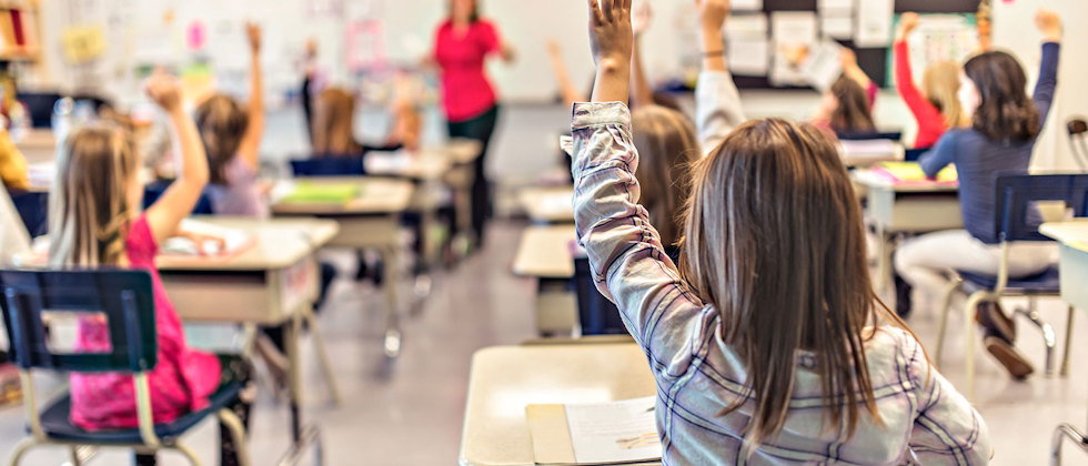 Lärare framför en klass som räcker upp handen