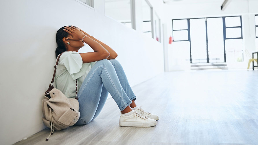 En elev som sitter i en tom skolkorridor och håller händerna för ansiktet