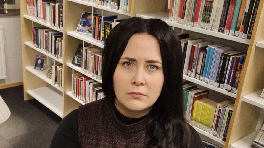 Ett foto av Magdalena Ivarsson, som tittar in i kameran med allvarlig min, bokhyllor i bakgrunden