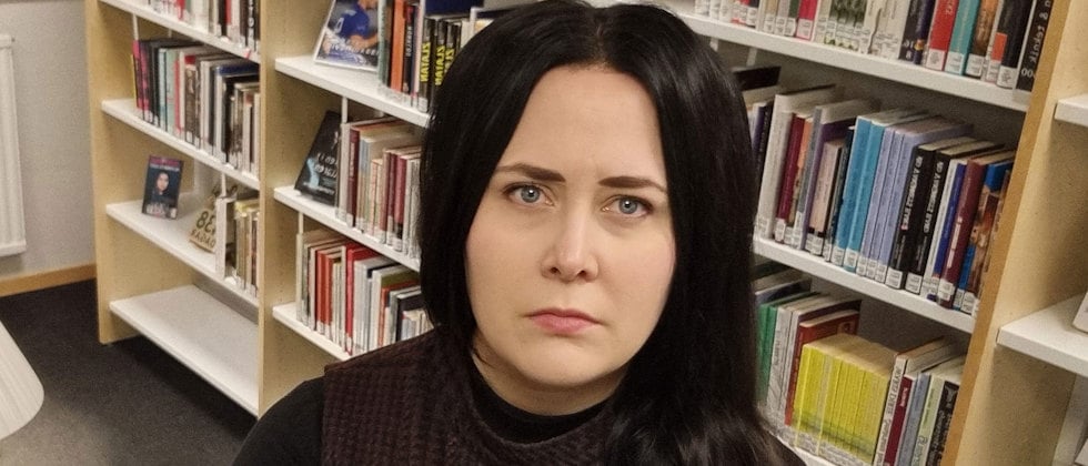 Ett foto av Magdalena Ivarsson, som tittar in i kameran med allvarlig min, bokhyllor i bakgrunden