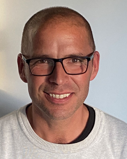 Ett porträtt av Mikael Engelhart, i vit tröja och svarta glasögon