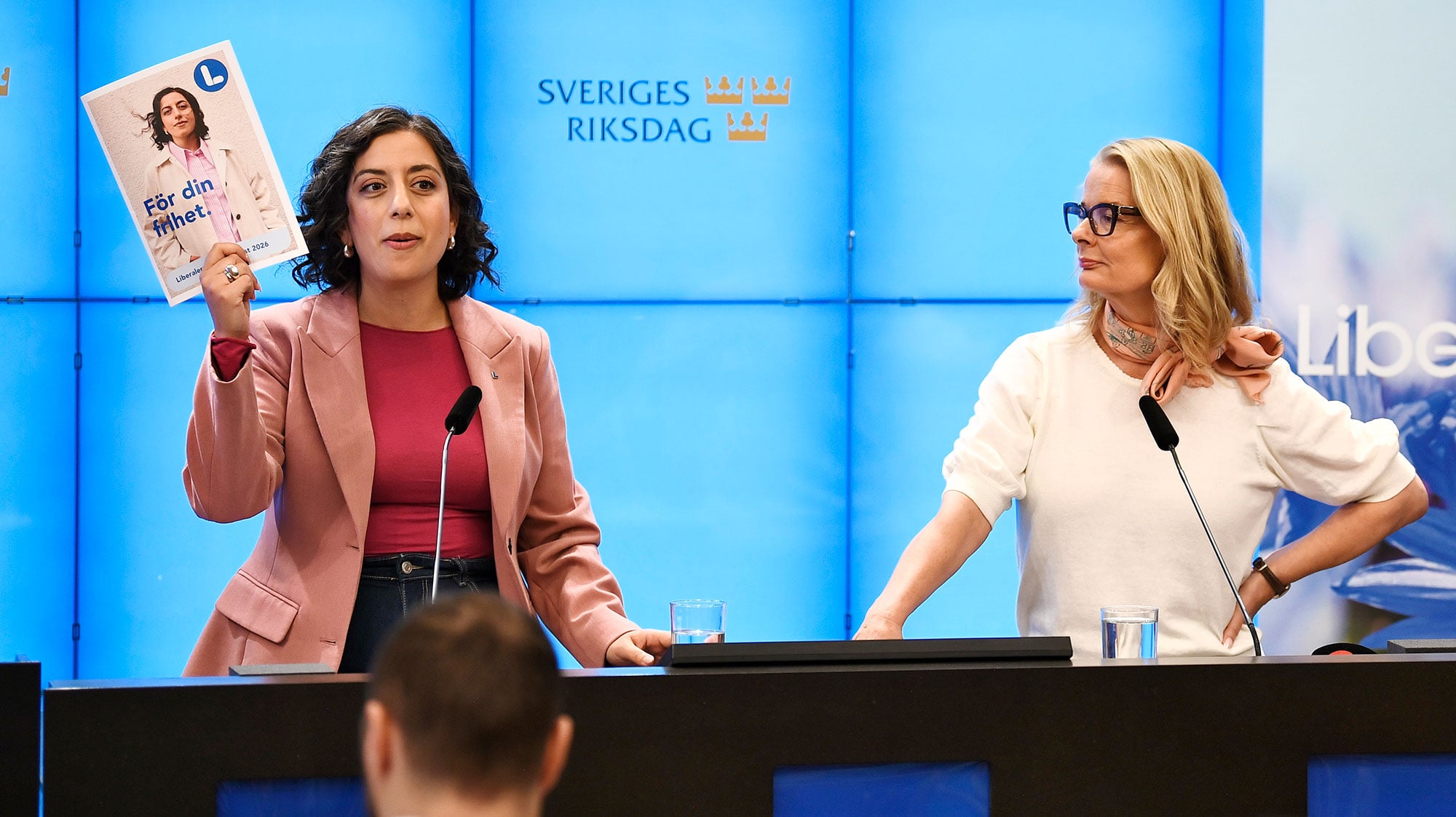 En bild på Simona Mohamsson som håller upp valmanifestet och Lotta Edholm, som tittar på Mohamsson.