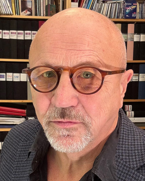 Ett porträtt av Nils-Eric Tedgård, mot en bakgrund av bokhyllor proppade med böcker