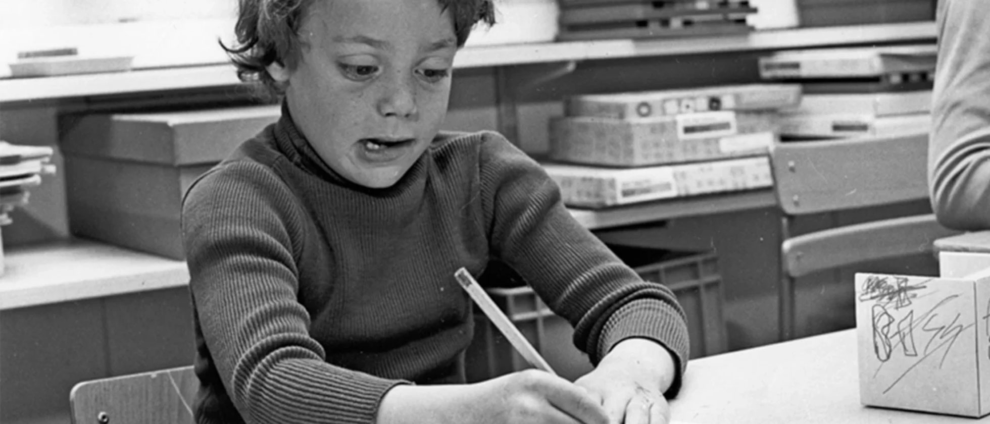 En svartvit bild av ett barn som sitter koncentrerat med pennan i handen