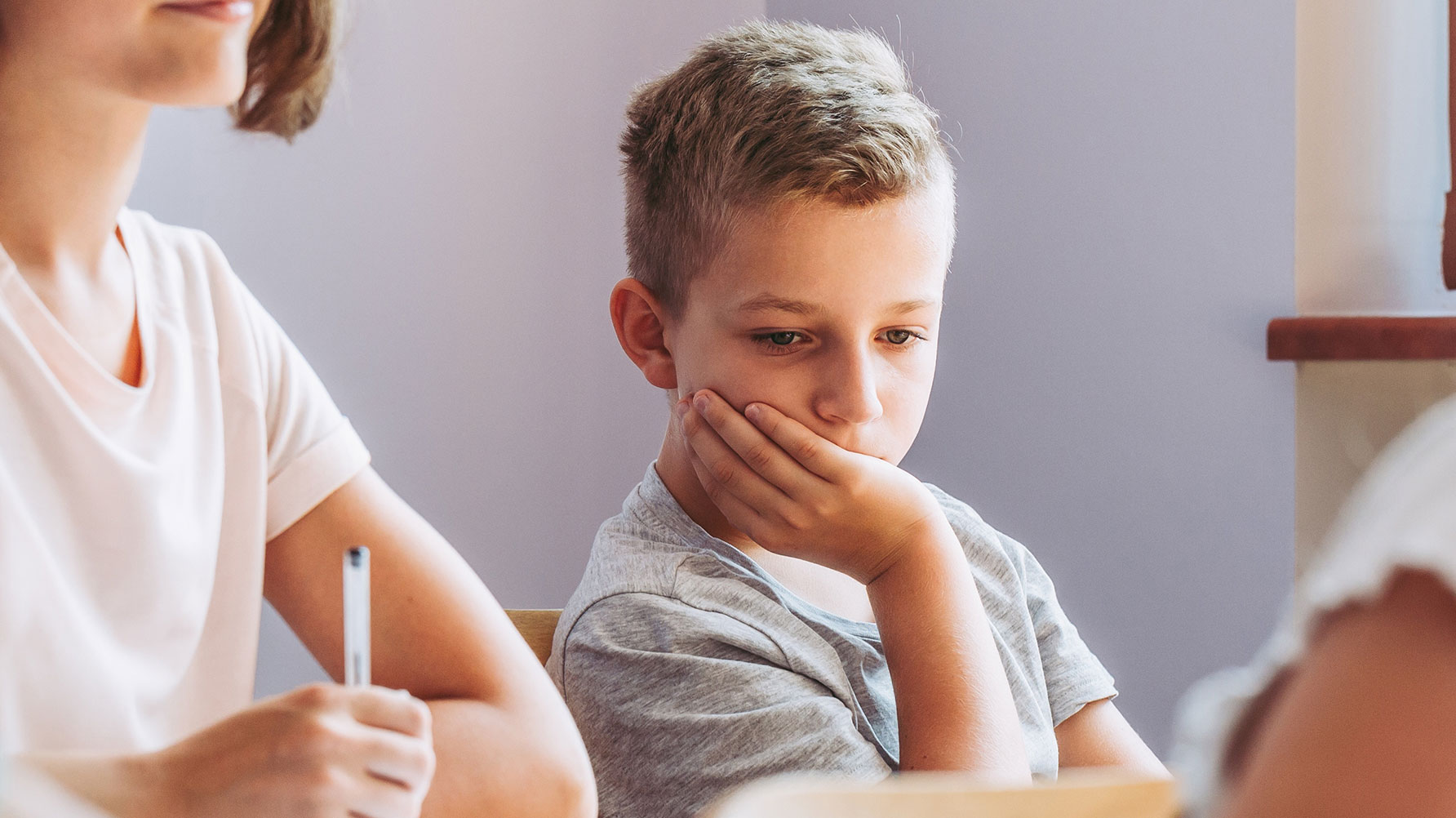 En genrebild ur ett klassrum, en pojke har huvudet i handen, han sitter i hörnet av klassrummet, blicken sluten.