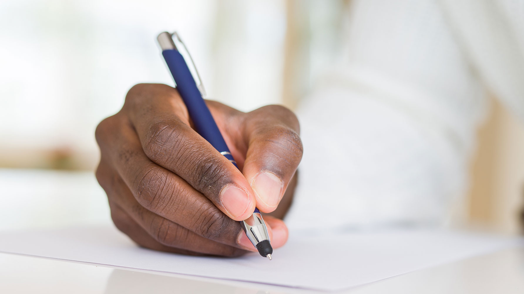 En genrebild av en hand som håller i en penna, över ett vitt pappersark