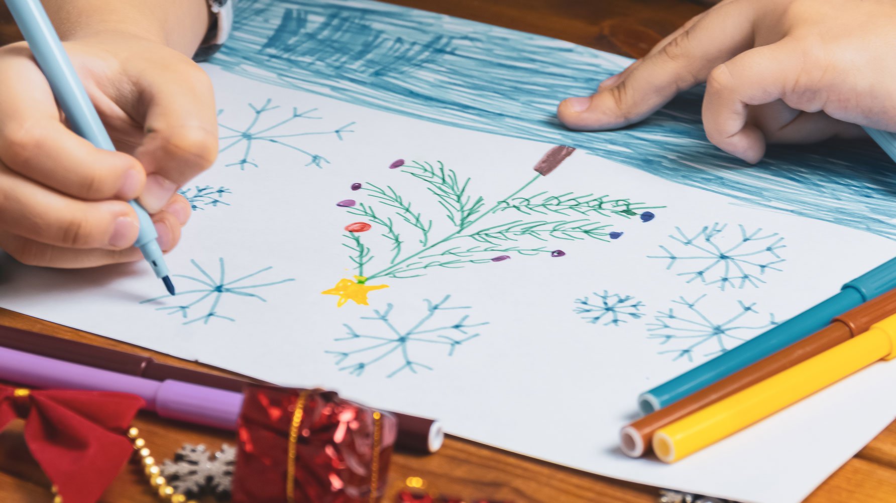 En närbild av en teckning av en julgran, man ser barnets händer när det ritar