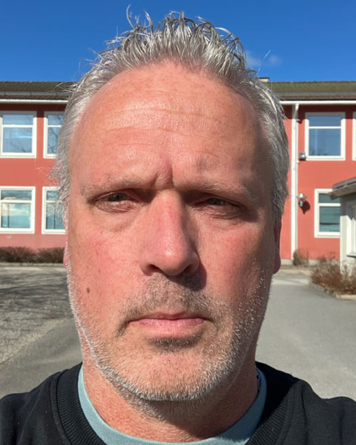 Ett porträtt av Thomas Ek, framför en skolbyggnad