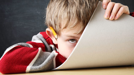 Ett barn i skolmiljö som håller ett papper framför ansiktet och ser uppgiven ut